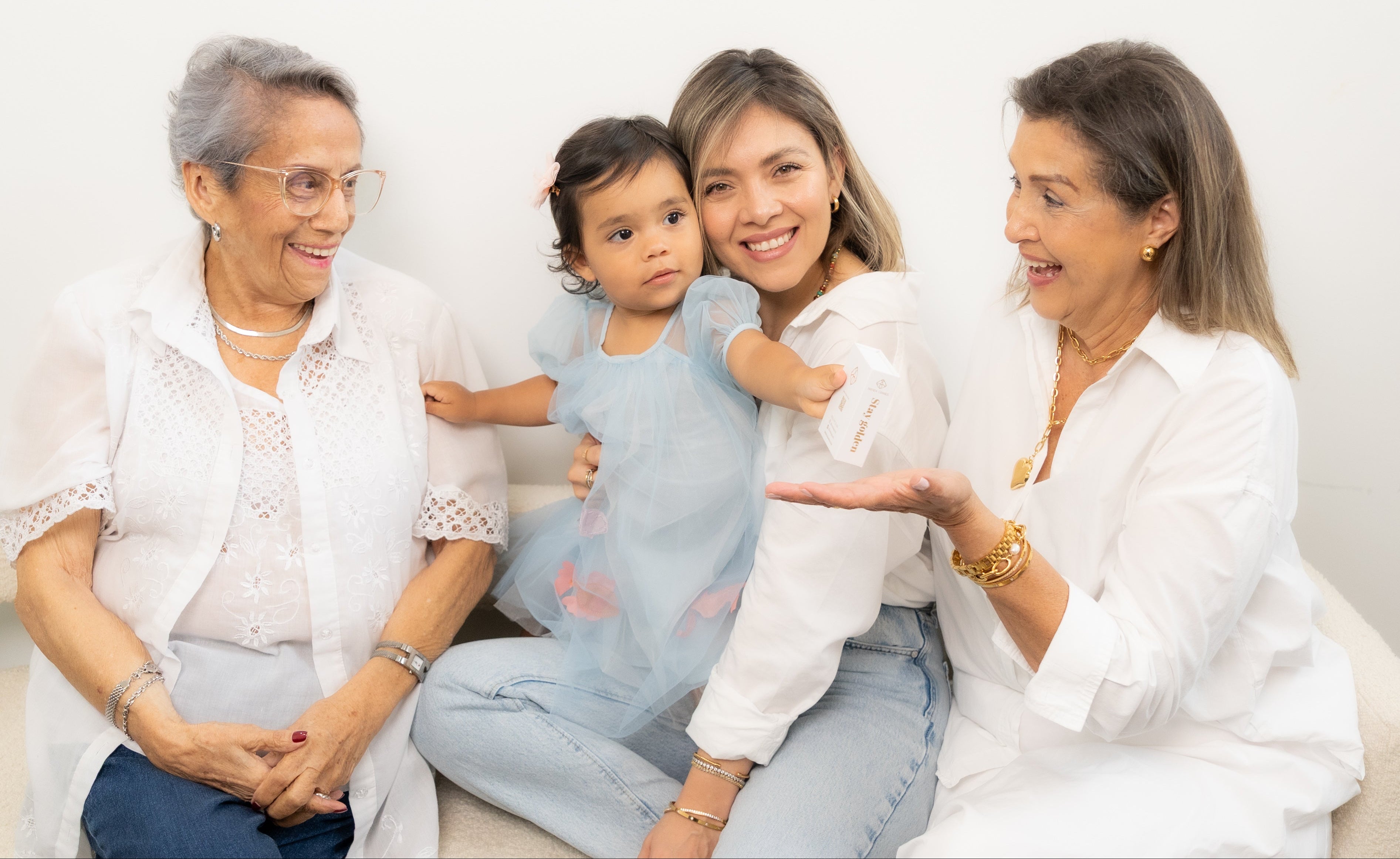 Four generations of women sitting together on a couch, smiling and holding a baby.